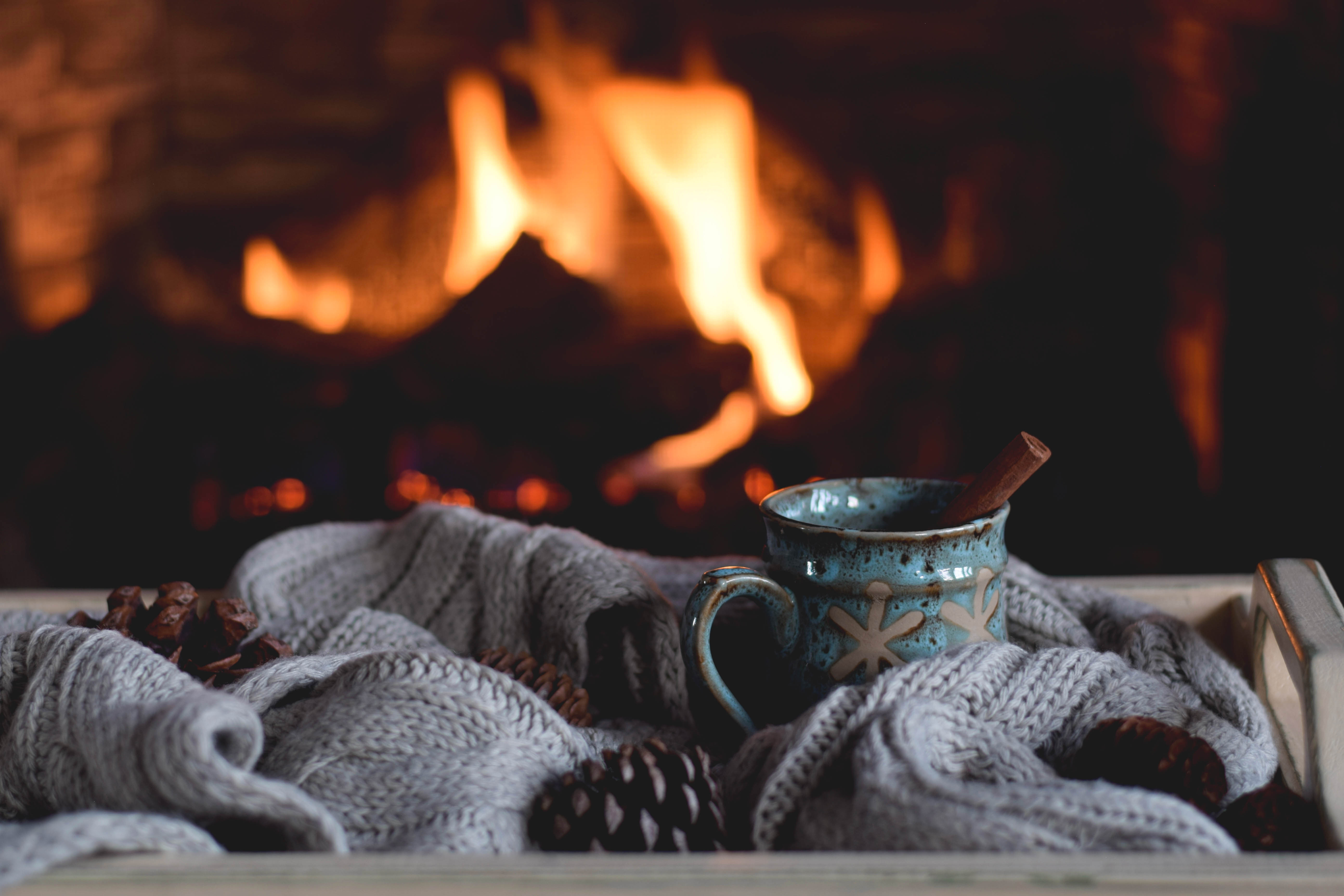 Close-up of a fireplace with a mug of hot cocoa with a cinnamon stick and a cozy blanket Close-up of a fireplace with a mug of hot cocoa with a cinnamon stick and a cozy blanket